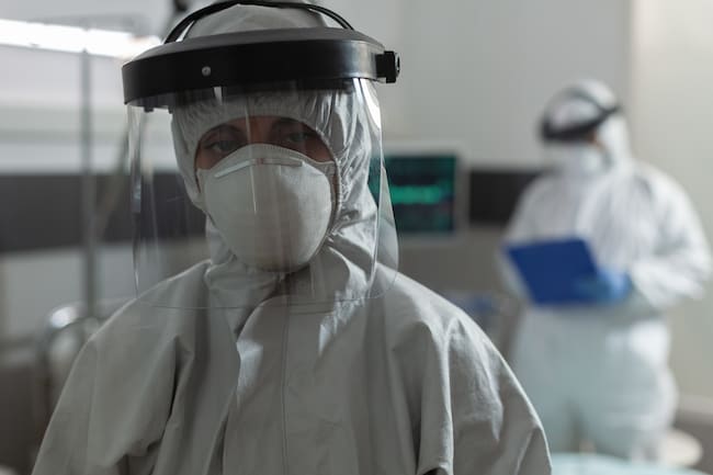 Медичний спеціаліст із маскою для обличчя, одягненим у комбінезон, під час спалаху пандемії коронавірусу, щоб запобігти зараженню covid-19. Лікар робить нотатки в буфер обміну говорити з пацієнтом.